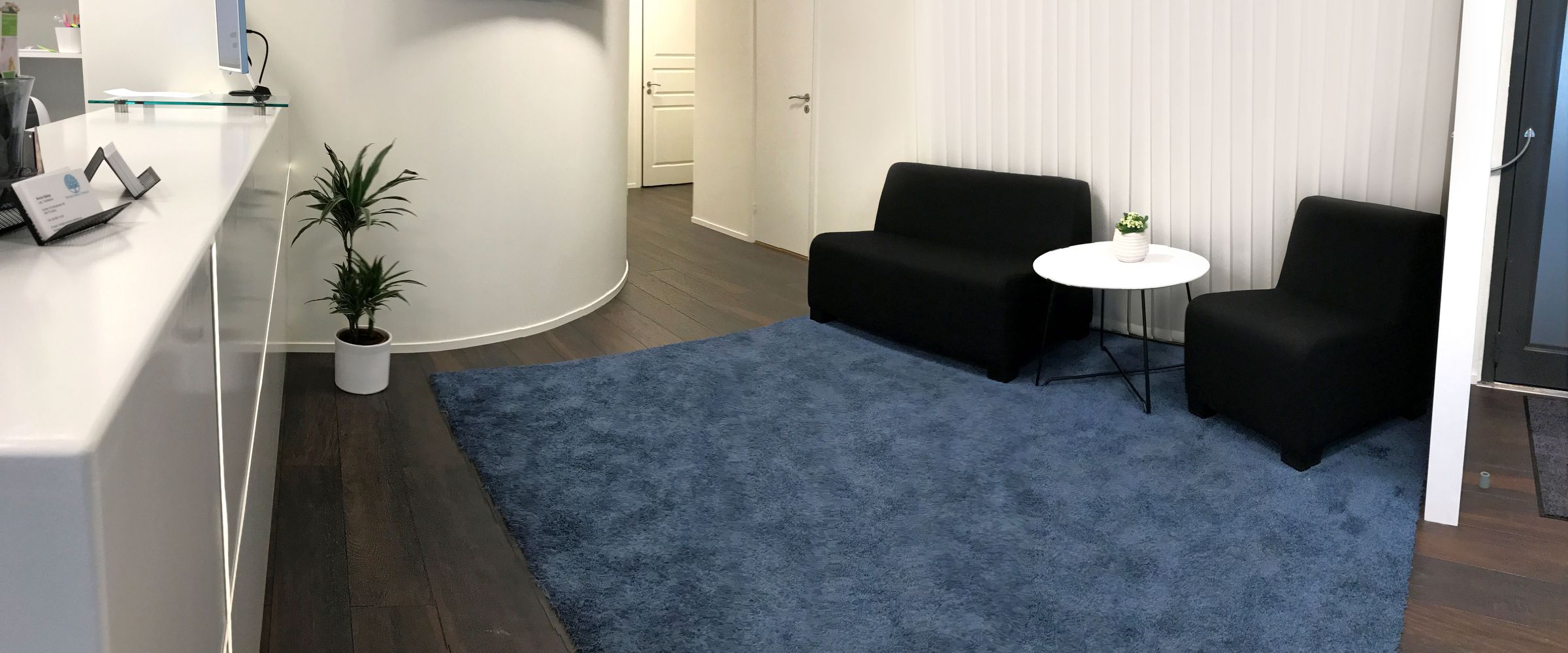 Väntrummet med svarta soffor och blå matta, sett från receptionen