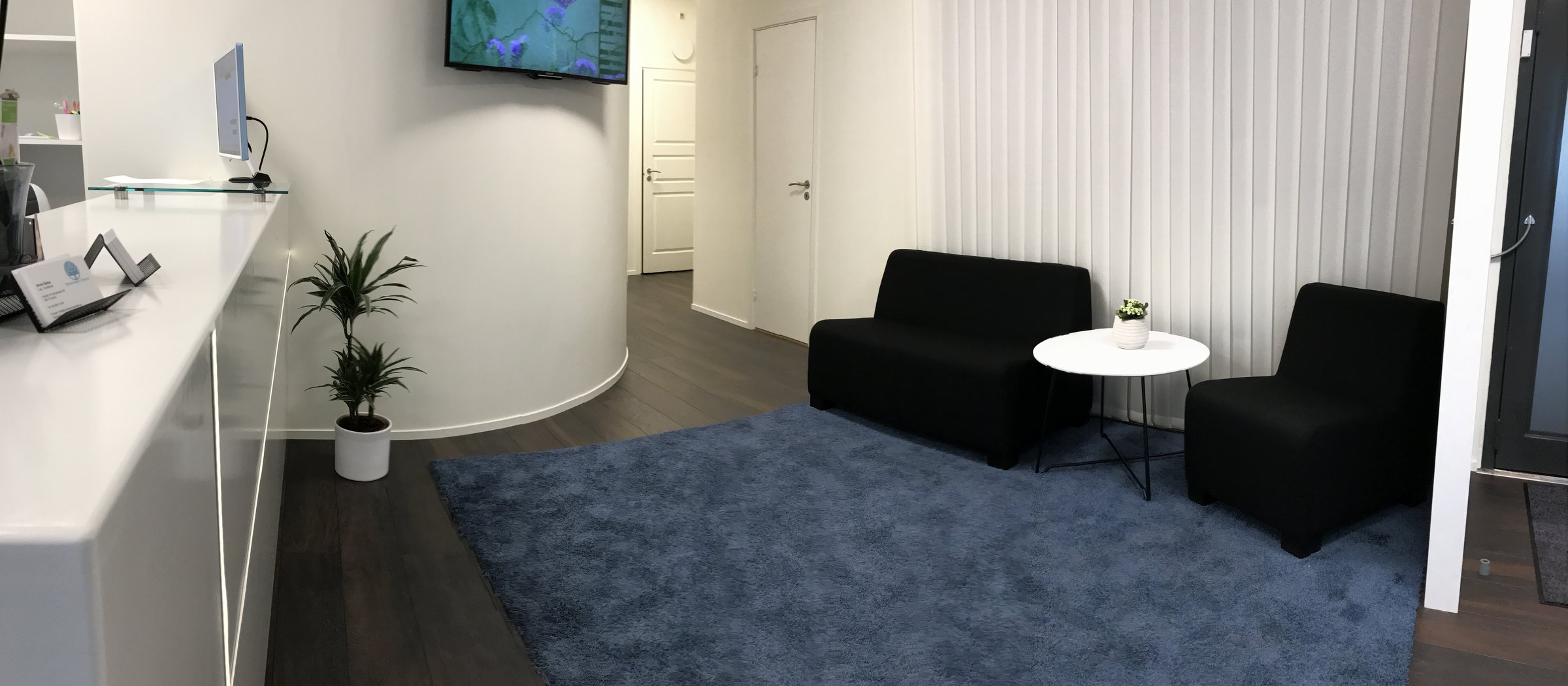 Väntrummet med svarta soffor och blå matta, sett från receptionsdisken